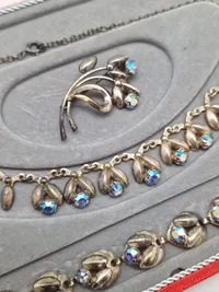 Smykkesæt bestående af halskæde, armbånd, øreringe og broche. Sættet er af sterlingsølv med isatte sten. Designet af Hans Siersbøl