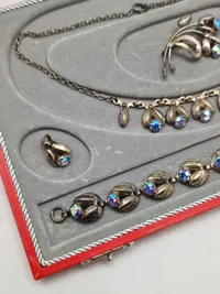 Smykkesæt bestående af halskæde, armbånd, øreringe og broche. Sættet er af sterlingsølv med isatte sten. Designet af Hans Siersbøl