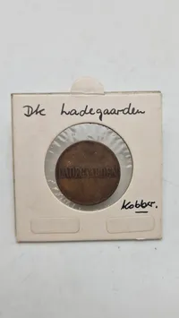 Originalt jernbliktegn fra Ladegården, som var Københavns største fattiggård og arbejdsanstalt. Tegnene blev brugt som intern valuta i marketenderiet, da de indsatte ikke måtte have rigtige penge.
