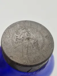 Blå spytflaske af glas med metalkapsel og gradueret skala i kubikcentimeter, som blev brugt til at opsamle spyt fra patienter med tuberkulose, især i perioden 1871-1920