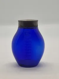Blå spytflaske af glas med metalkapsel og gradueret skala i kubikcentimeter, som blev brugt til at opsamle spyt fra patienter med tuberkulose, især i perioden 1871-1920