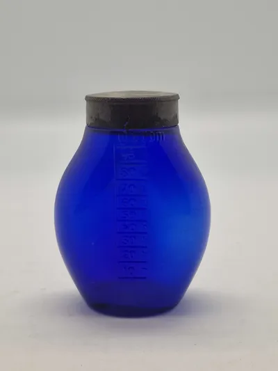 Blå spytflaske af glas med metalkapsel og gradueret skala i kubikcentimeter, som blev brugt til at opsamle spyt fra patienter med tuberkulose, især i perioden 1871-1920