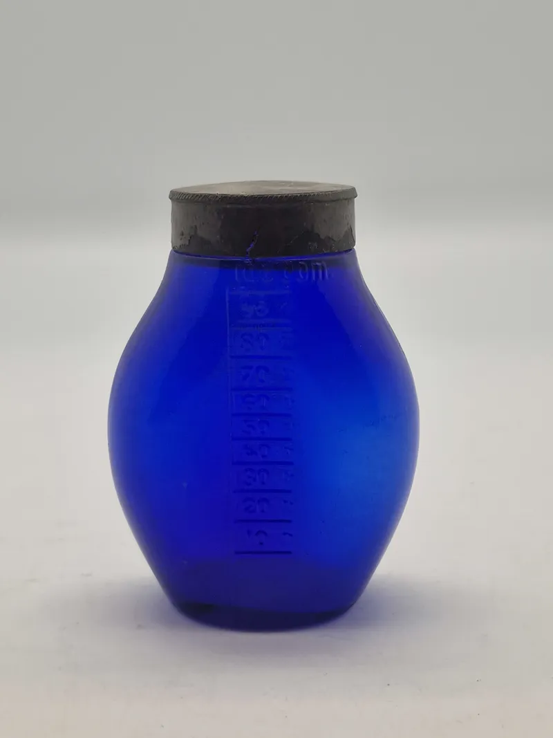 Blå spytflaske af glas med metalkapsel og gradueret skala i kubikcentimeter, som blev brugt til at opsamle spyt fra patienter med tuberkulose, især i perioden 1871-1920