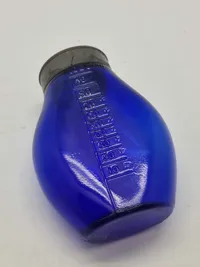 Blå spytflaske af glas med metalkapsel og gradueret skala i kubikcentimeter, som blev brugt til at opsamle spyt fra patienter med tuberkulose, især i perioden 1871-1920