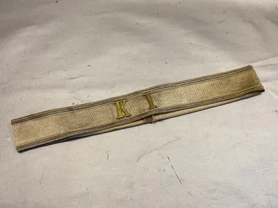 Kasketbånd med isatte metalbogstaver “KI”