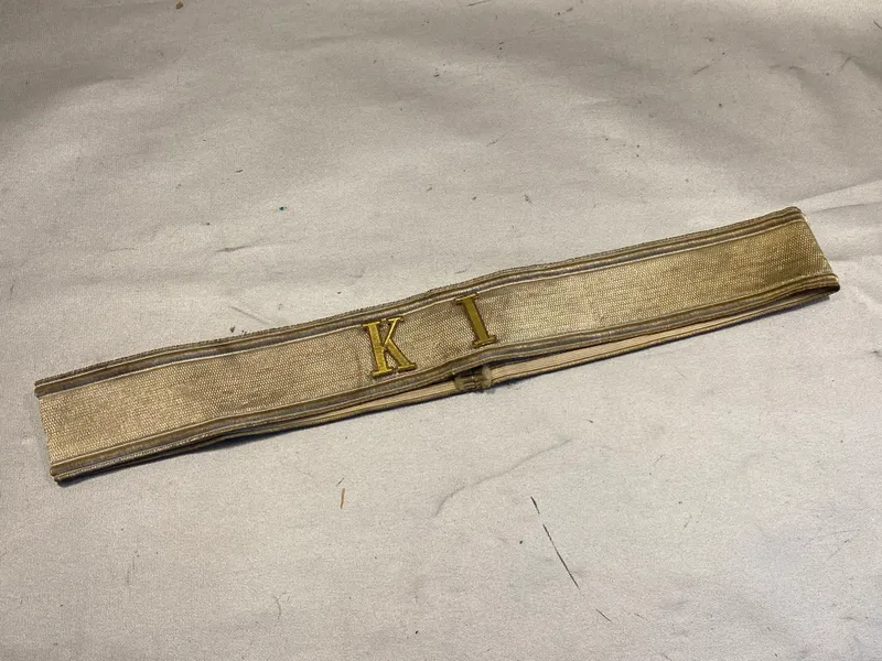Kasketbånd med isatte metalbogstaver “KI”