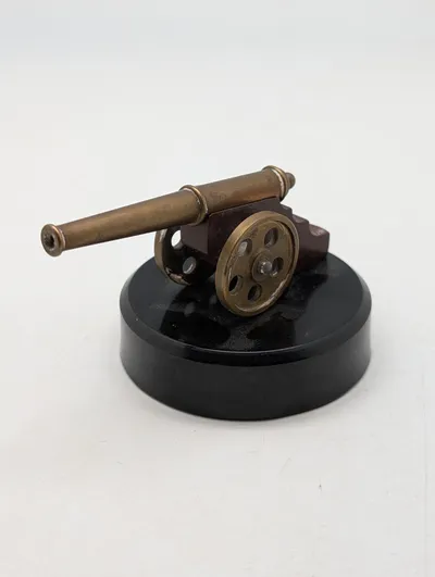 Miniature messingkanon på sort rund sokkel