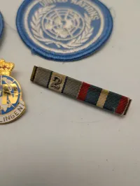 Samling af FN-militaria: To stofmærker, emaljenål og ordensbånd