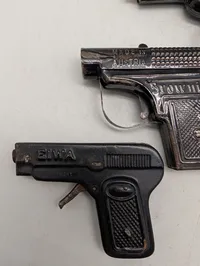 Tre antikke legetøjspistoler i metal, herunder O'les mains og D.R.G.M.