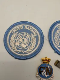 Samling af FN-militaria: To stofmærker, emaljenål og ordensbånd