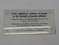 Antikt emaljeskilt med togtoilet-instruktioner på fire sprog DSB