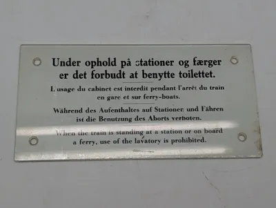 Antikt emaljeskilt med togtoilet-instruktioner på fire sprog DSB
