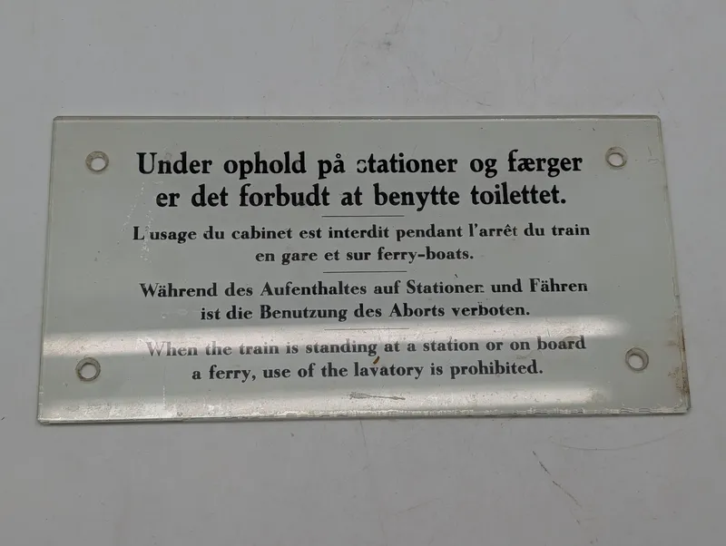 Antikt emaljeskilt med togtoilet-instruktioner på fire sprog DSB