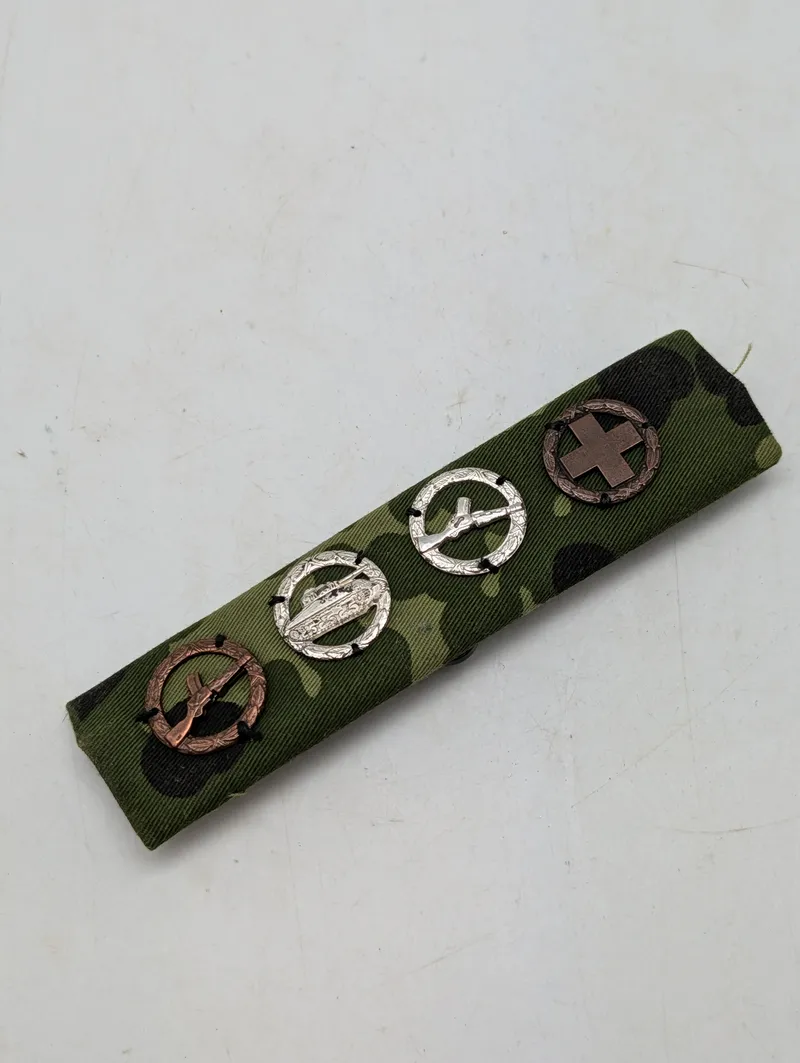 Militær bånd med fire færdighedstegn på camouflagebund