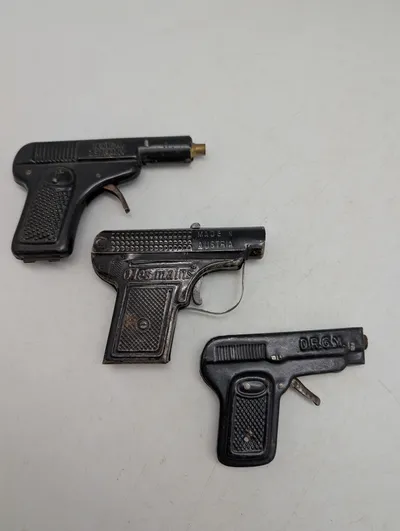 Tre antikke legetøjspistoler i metal, herunder O'les mains og D.R.G.M.